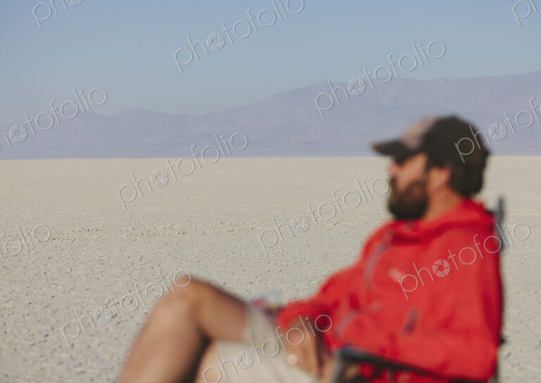 Man sitting in chair in vast, barren desert, blurred focus