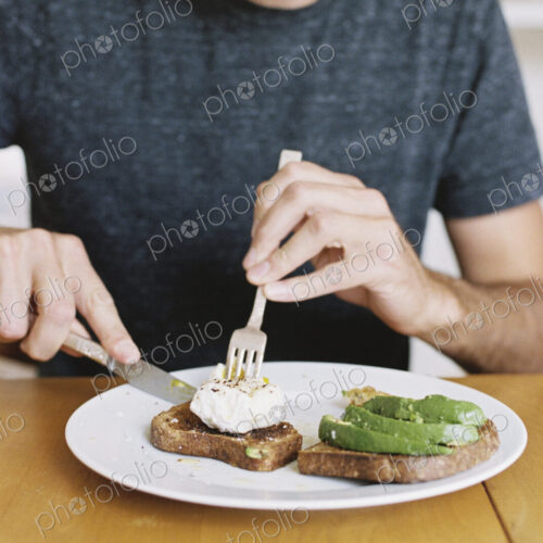 Man sitting in front of a plate of food at a table, eating.