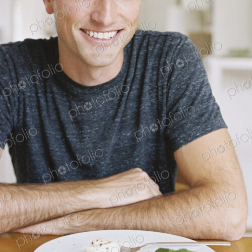 Man sitting in front of a plate of food at a table, looking at camera, smiling.