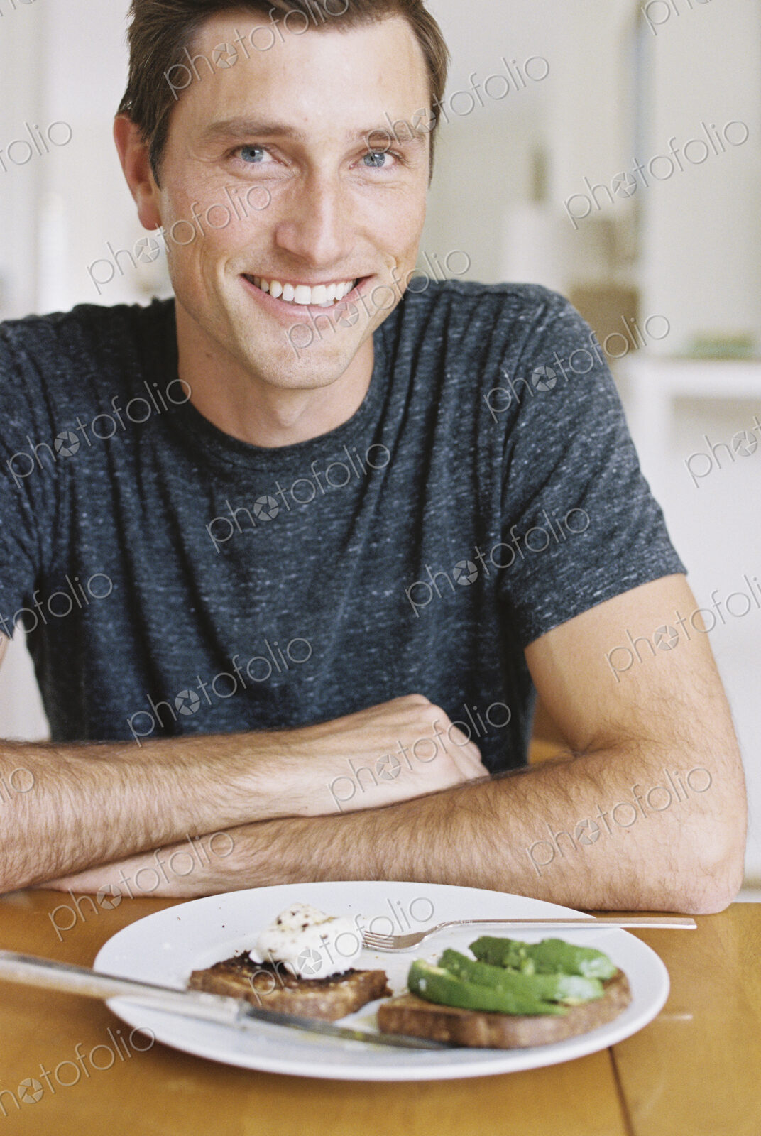 Man sitting in front of a plate of food at a table, looking at camera, smiling.