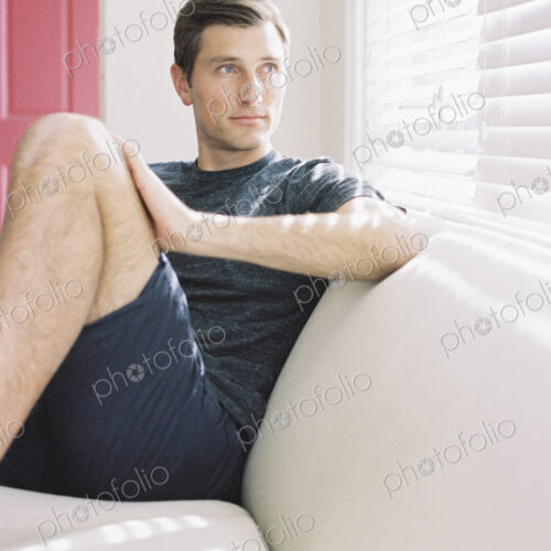 Man sitting on a sofa by a window, relaxing.