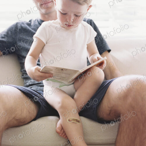 Man sitting on a sofa with his son, holding a book, reading.