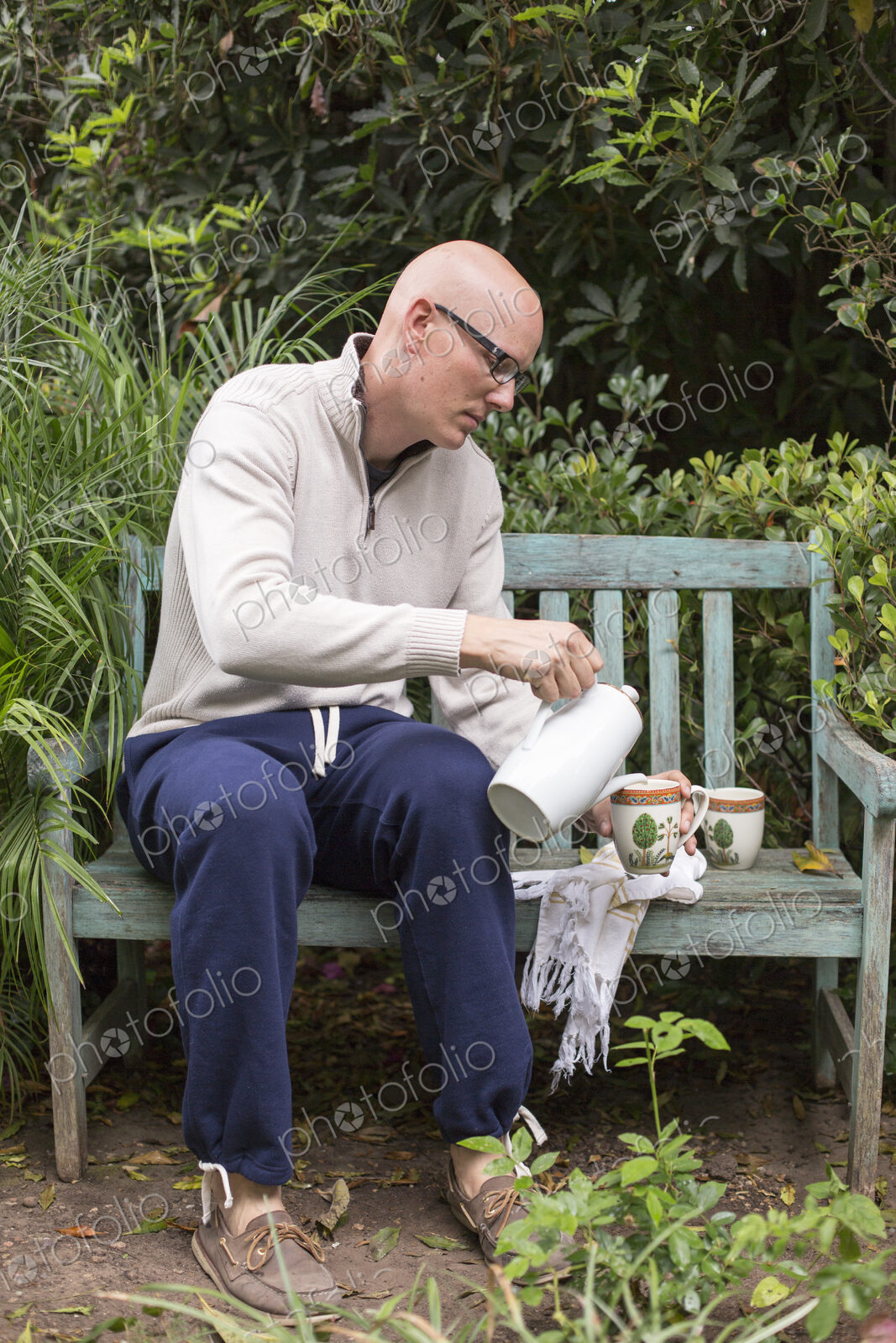Man sitting on a wooden bench in a garden, pouring a cup of coffee.