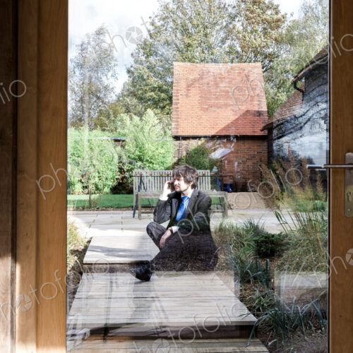 Man sitting on path to house, seen through glass door. Man sitting on path to house, seen through glass door.
