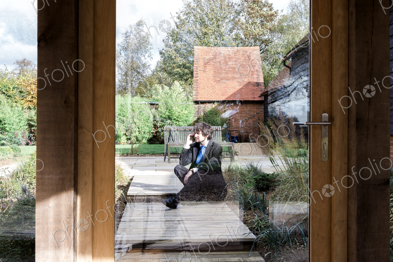 Man sitting on path to house, seen through glass door.