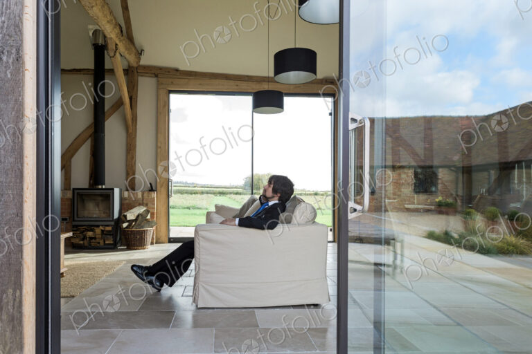 Man sitting on sofa in living room of converted barn house.