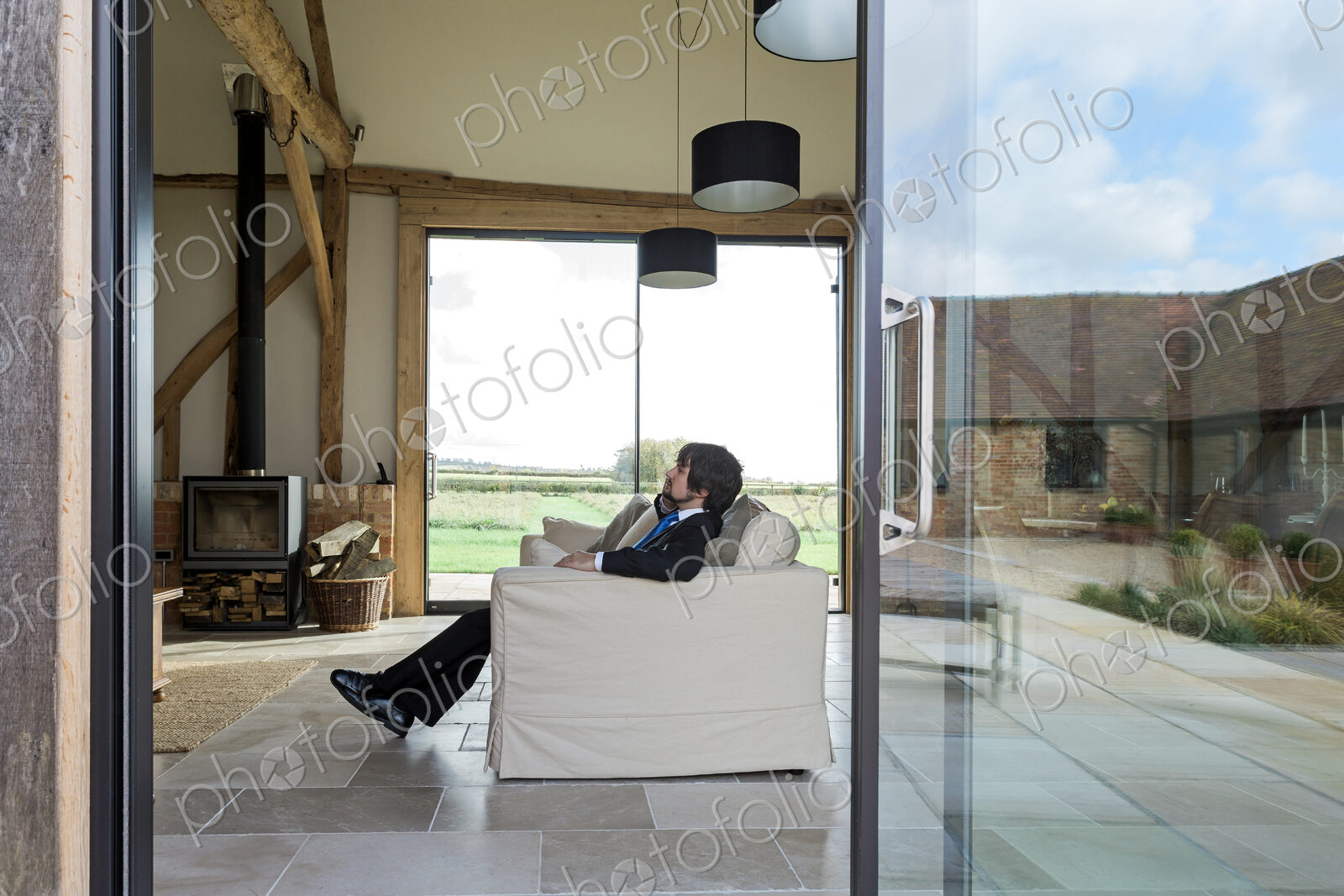 Man sitting on sofa in living room of converted barn house.
