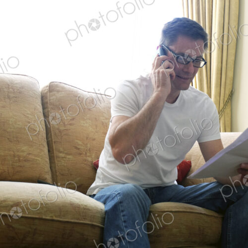 Man sitting on sofa making phone call holding paperwork. Man sitting on sofa making phone call holding paperwork.