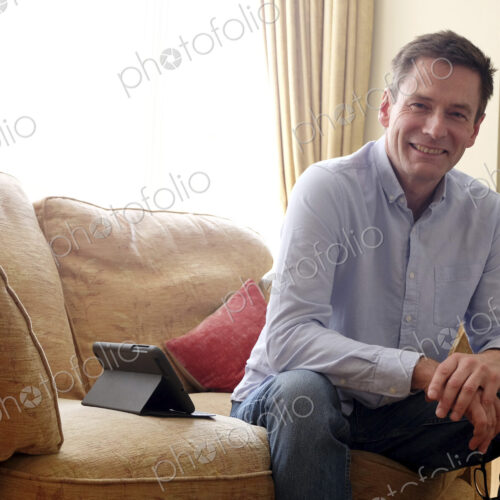 Man sitting on sofa smiling at camera.