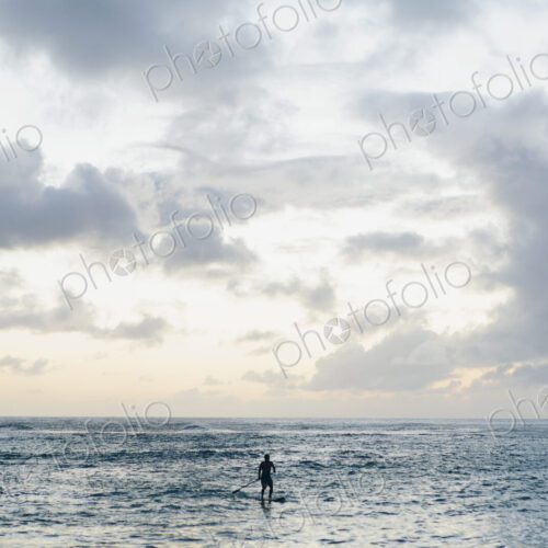 Man stand up paddling in calm waters at dusk