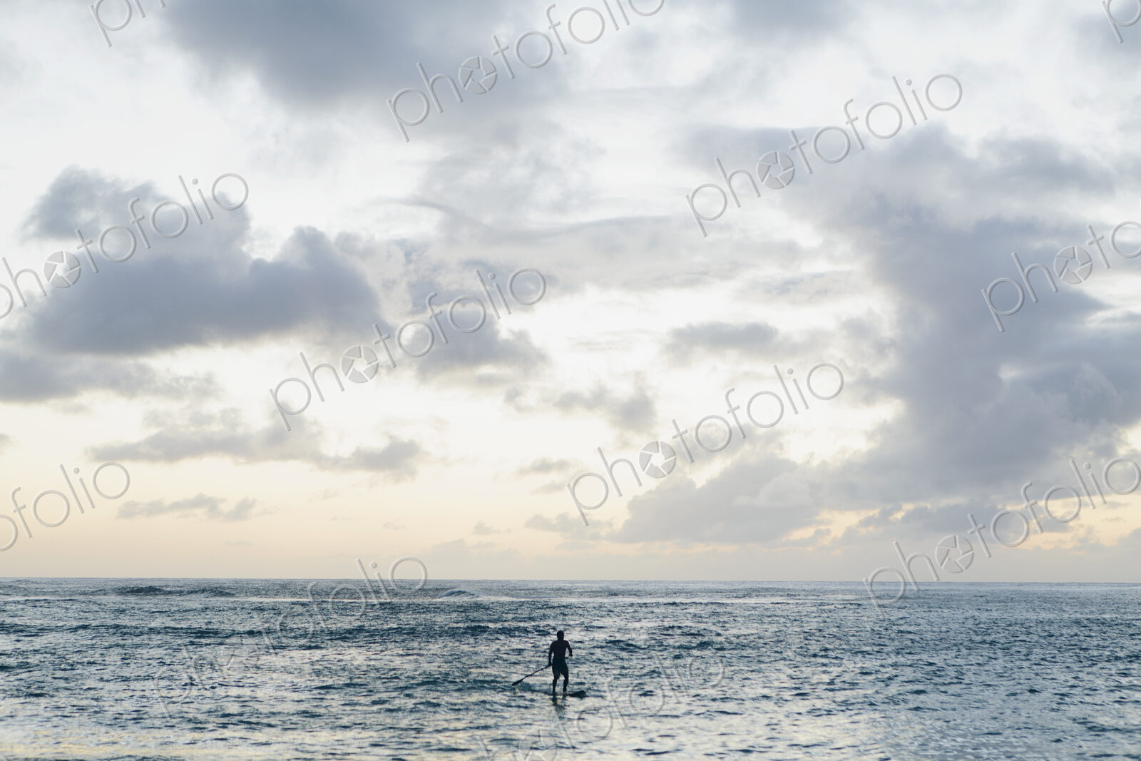 Man stand up paddling in calm waters at dusk