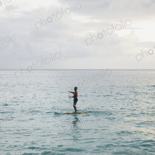 Man stand up paddling in calm waters at dusk