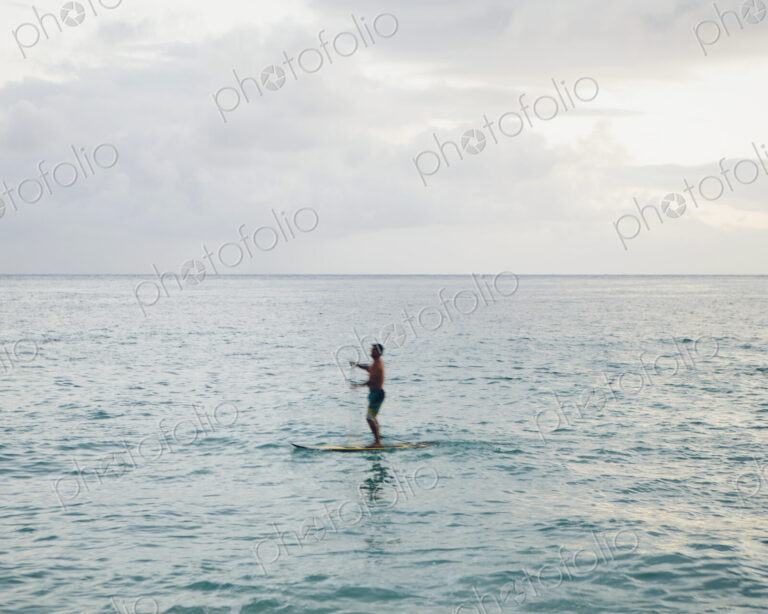 Man stand up paddling in calm waters at dusk