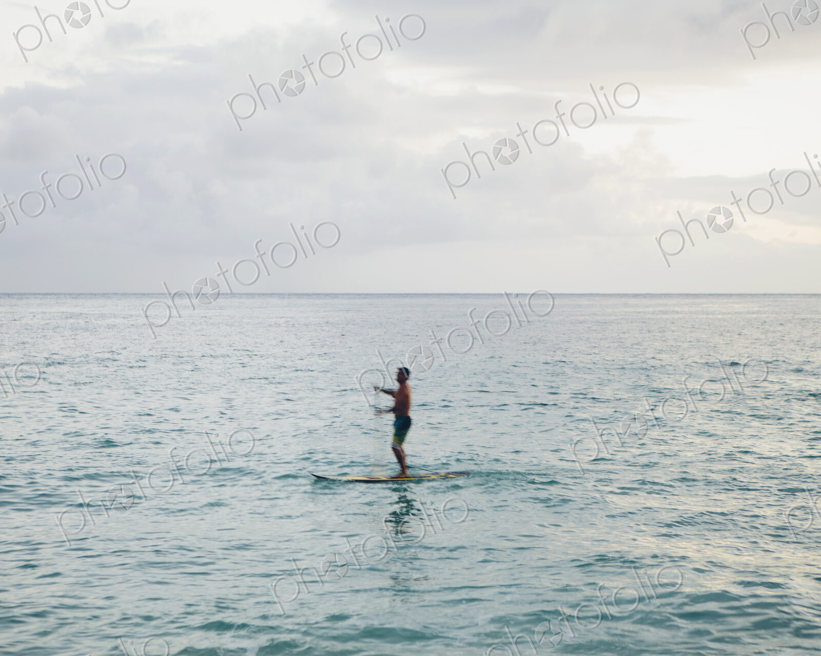 Man stand up paddling in calm waters at dusk