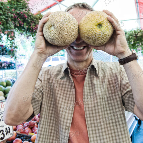 Man standing at a farm stall, covering his eyes with two fresh melons, smiling at camera. Man standing at a farm stall, covering his eyes with two fresh melons, smiling at camera.