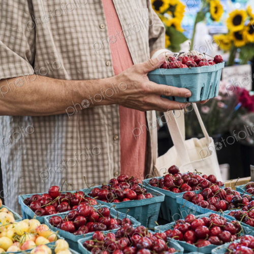 Man standing at stall, holding punnet with fresh cherries at a fruit and vegetable market. Man standing at stall, holding punnet with fresh cherries at a fruit and vegetable market.