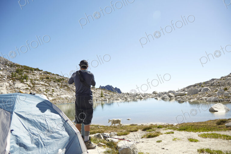 Man standing at tent at campsite near rural lake