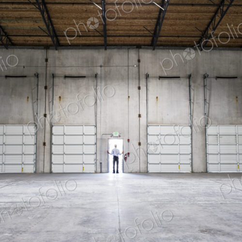 Man standing doorway of new warehouse waiting for the arrival of the first truck wiith… Man standing doorway of new warehouse waiting for the arrival of the first truck wiith…