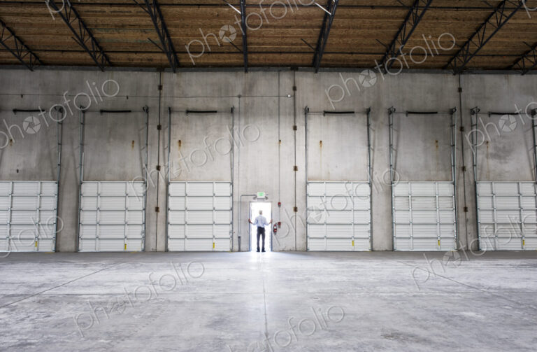 Man standing doorway of new warehouse waiting for the arrival of the first truck wiith…