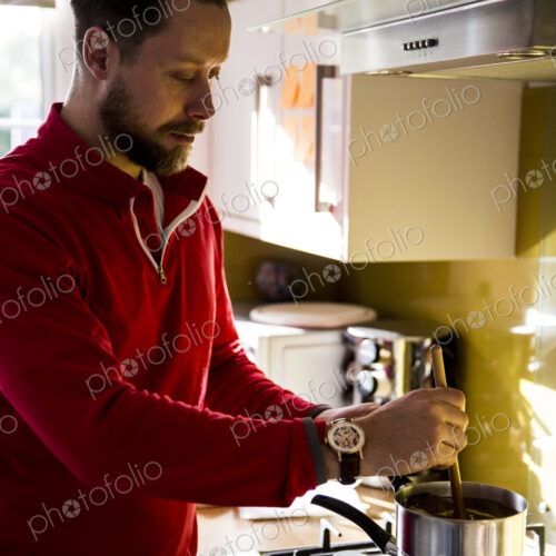 Man standing in a domestic kitchen, making jar candles. Man standing in a domestic kitchen, making jar candles.
