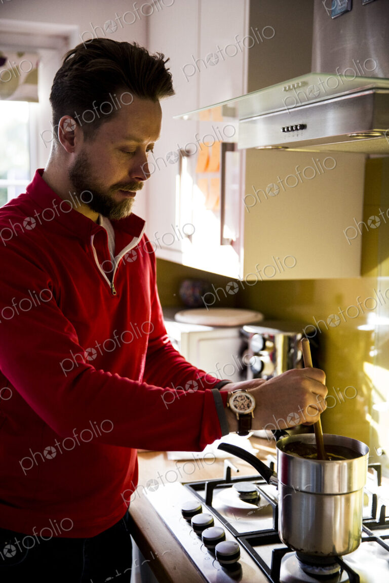 Man standing in a domestic kitchen, making jar candles.