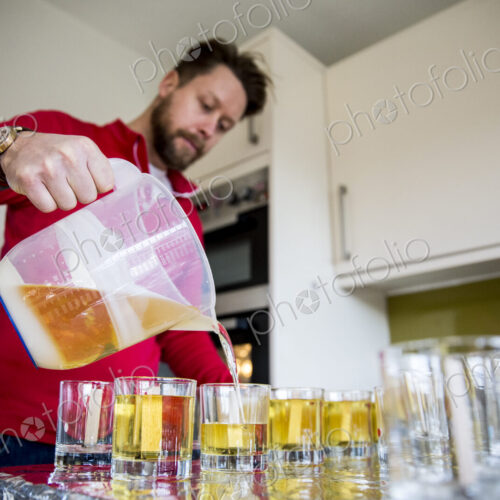 Man standing in a domestic kitchen, making jar candles.