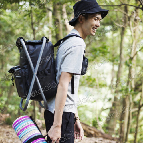 Man standing in a forest, carrying a picnic rug and backpack.