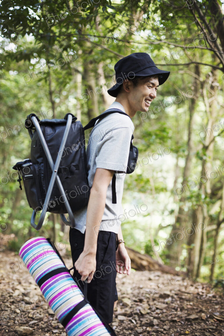 Man standing in a forest, carrying a picnic rug and backpack.