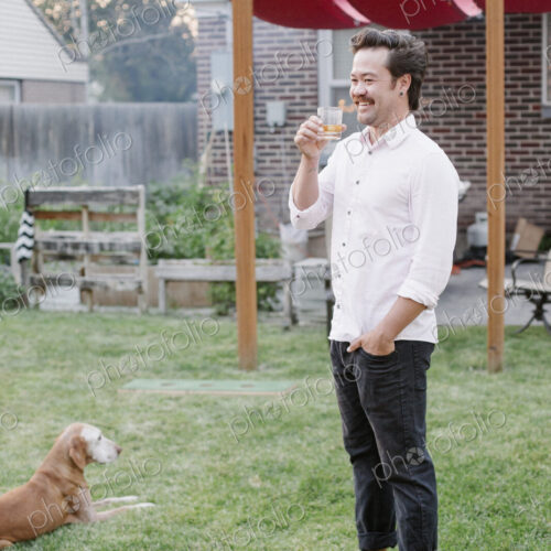 Man standing in a garden, enjoying a drink, a dog lying on the grass beside him. Man standing in a garden, enjoying a drink, a dog lying on the grass beside him.