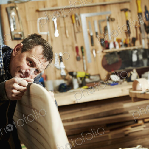 Man standing in a workshop inspecting closely the edge of a wooden surfboard. Man standing in a workshop inspecting closely the edge of a wooden surfboard.