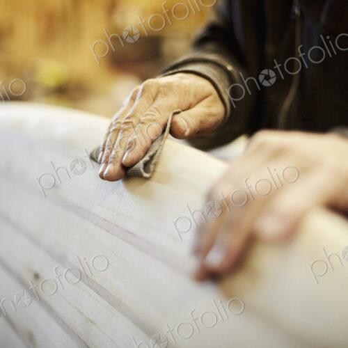 Man standing in a workshop sanding the edge of a wooden surfboard. Man standing in a workshop sanding the edge of a wooden surfboard.