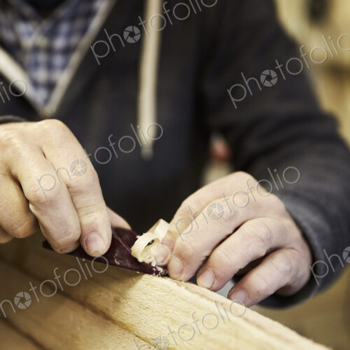 Man standing in a workshop, shaping a wooden surfboard using a hand held plane. Man standing in a workshop, shaping a wooden surfboard using a hand held plane.