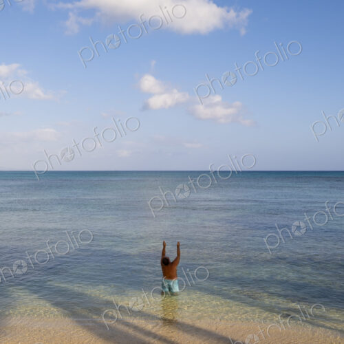 Man standing in shallow tropical water with arms raised, Waikiki, Honolulu, Oahu Man standing in shallow tropical water with arms raised, Waikiki, Honolulu, Oahu