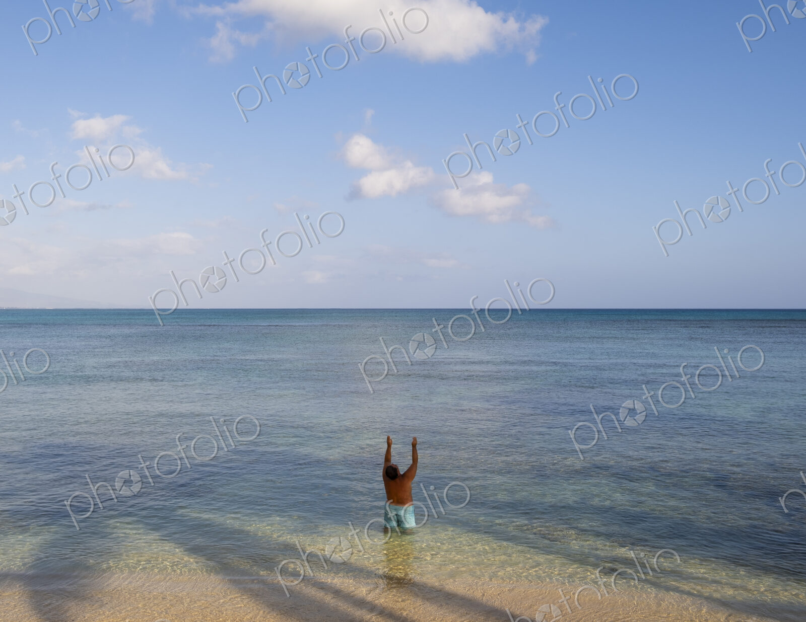 Man standing in shallow tropical water with arms raised, Waikiki, Honolulu, Oahu