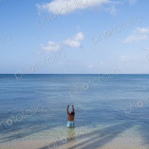 Man standing in shallow tropical water with arms raised, Waikiki, Honolulu, Oahu Man standing in shallow tropical water with arms raised, Waikiki, Honolulu, Oahu