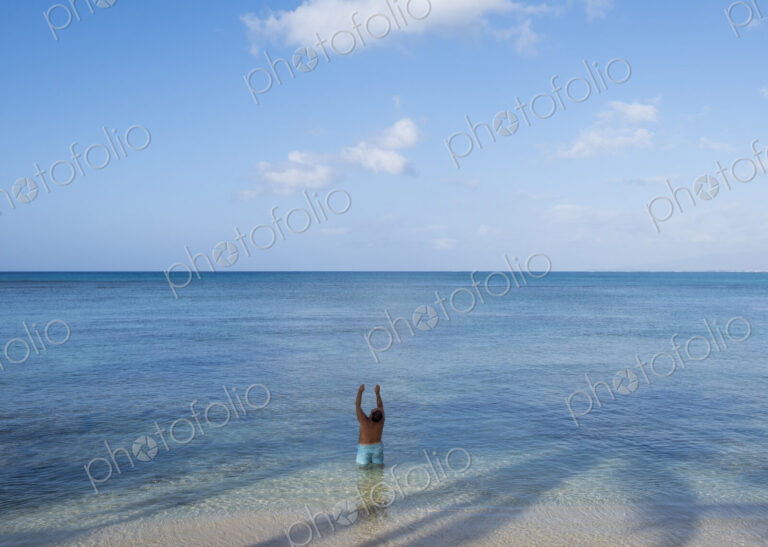 Man standing in shallow tropical water with arms raised, Waikiki, Honolulu, Oahu
