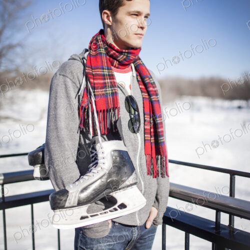 Man standing in snow with ice skates hanging around his neck.