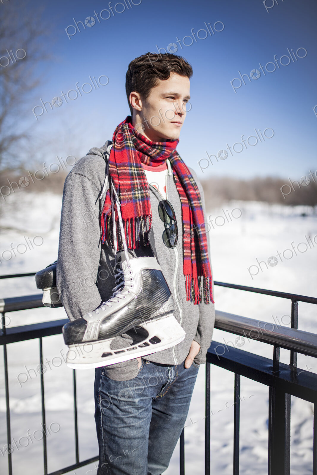 Man standing in snow with ice skates hanging around his neck.