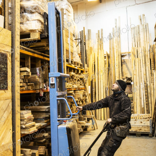 Man standing in warehouse using forklift to move pallet of wood off a shelf. Man standing in warehouse using forklift to move pallet of wood off a shelf.