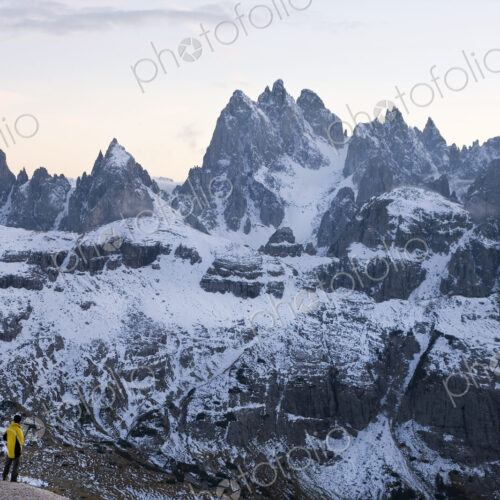 Man standing next to tent pitched amidst snow-covered mountain range.
