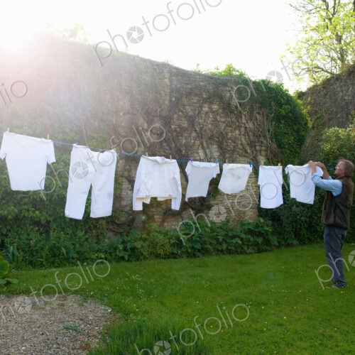 Man standing on a lawn in a garden, hanging up laundry on washing line. Man standing on a lawn in a garden, hanging up laundry on washing line.