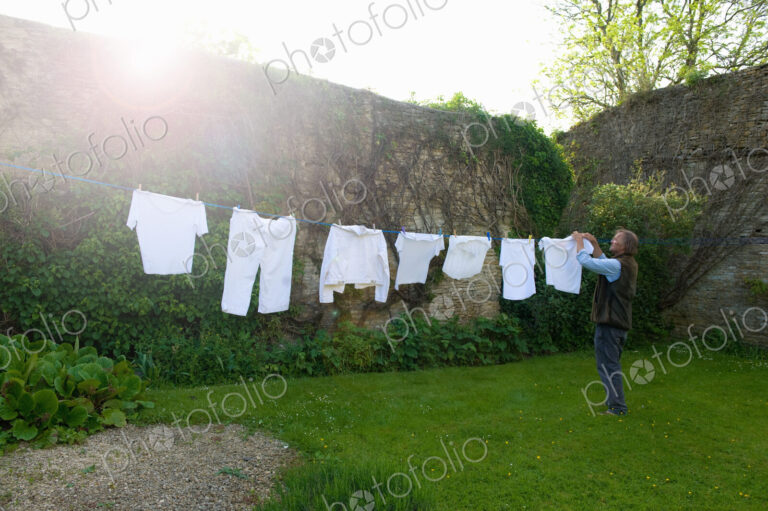 Man standing on a lawn in a garden, hanging up laundry on washing line.
