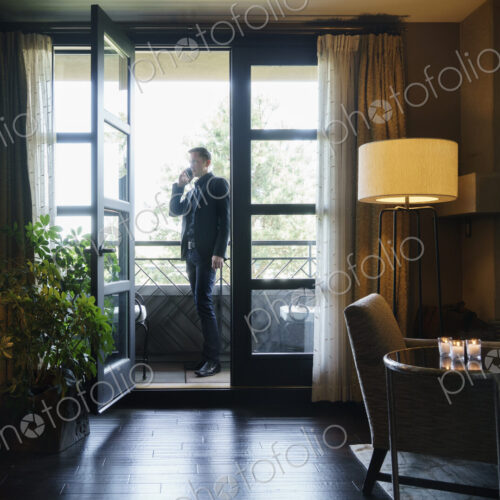 Man standing on hotel balcony talking on mobile telephone.