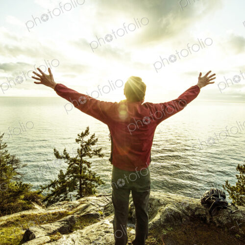 Man standing with arms outstretched on rocks over ocean Man standing with arms outstretched on rocks over ocean