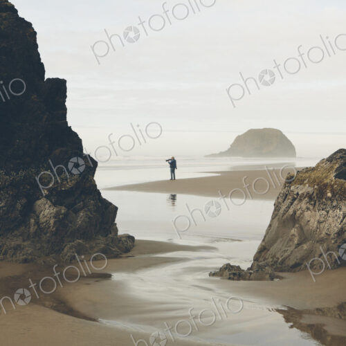 Man taking photos on beach at low tide, Arcadia Beach State Park, Oregon Man taking photos on beach at low tide, Arcadia Beach State Park, Oregon