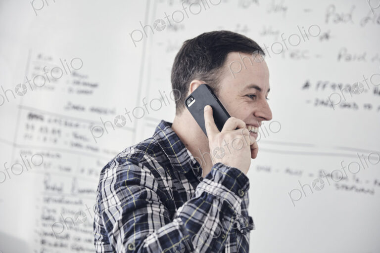 Man talking on mobile phone in an office, by a whiteboard.