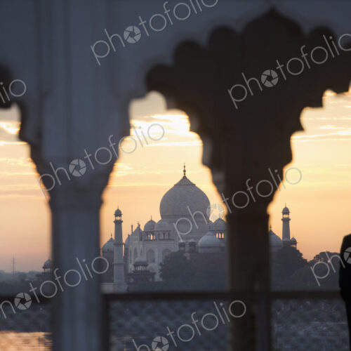 Man under a scalloped arch on balcony at sunset, Taj Mahal palace and mausoleum in the… Man under a scalloped arch on balcony at sunset, Taj Mahal palace and mausoleum in the…