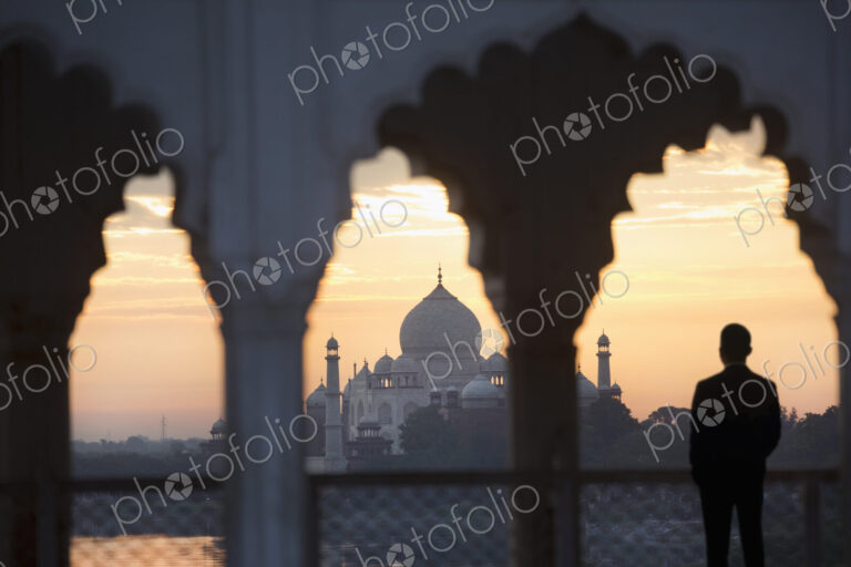 Man under a scalloped arch on balcony at sunset, Taj Mahal palace and mausoleum in the…