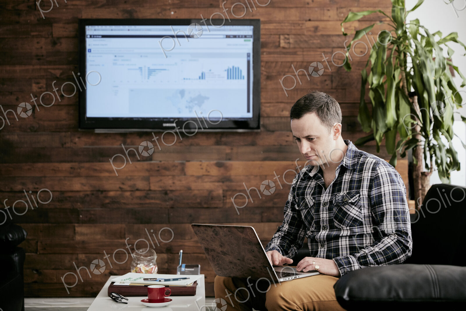 Man using a laptop balanced on his knee, sitting on sofa in a small office.