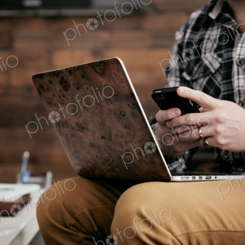 Man using a mobile phone and balancing his laptop on his knee.